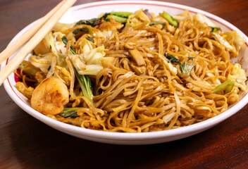 Fried noodle with chicken and vegetables in a white bowl on a wooden table. After edits.