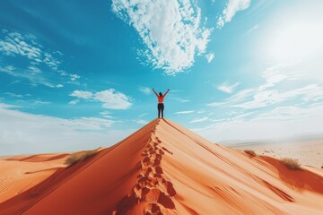 A person is standing on a sand dune, looking up at the sky