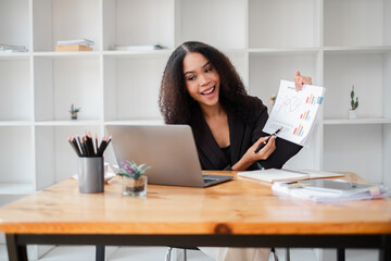 Joyful businesswoman shares a financial report, gesturing positively towards her laptop in an office setting.