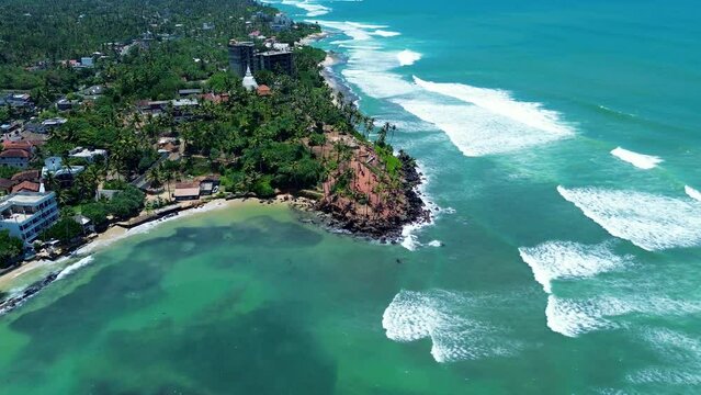 Aerial drone of Coconut tree hill bay palm plantation on headland coastline with local town village Indian ocean waves Mirissa Point Sri Lanka Asia