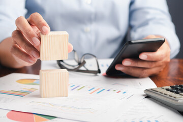 Businessman holding a mobile phone, and wooden cubes are on the desk.