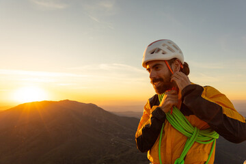 A man in a yellow jacket is adjusting his harness. The sun is setting behind him, casting a warm...