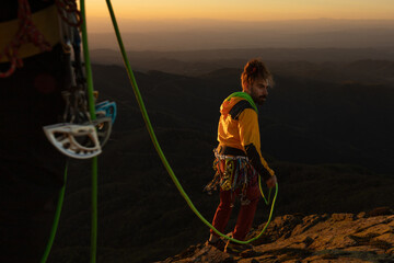 A man in a yellow jacket is climbing a mountain with a green rope