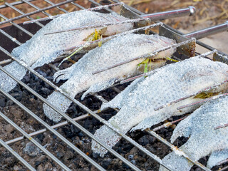 Grilled salted tilapia fish on charcoal grill at the market