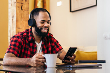 African american man using smartphone while having coffee at home