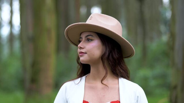 Woman looks thoughtfully around the landscape, then looks into the shot and begins to smile. Seductive look of a lady in a hat and white jacket