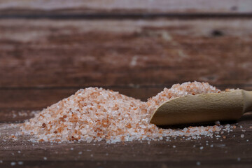 Fototapeta na wymiar close-up of a pile of pink himalayan salt in a wooden spoon on a wooden table with copy space