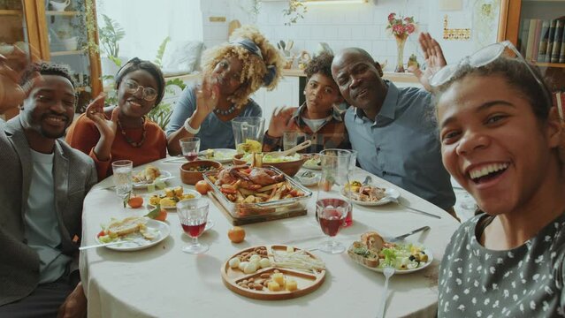 Big African American family looking at camera, happily smiling and waving while taking photos together on holiday dinner at home