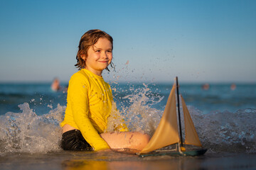 Little kid boy enjoying summer vacation by the sea. A cute little boy playing with a toy ship on the beach on a warm sunny summer day. Summer Holidays at sea. Kid playing with toy sailing boat. - 786845371
