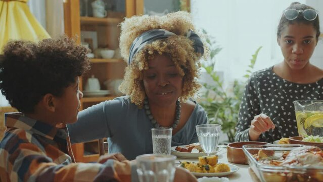 Loving Black Mother Talking With Little Son When Sitting Together At Dinner Table And Eating Meal During Family Celebration At Home