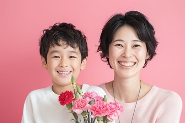 A carnations bouquet in front of the face, a smiling Japanese boy and his mother holding carnation flowers on a pink background for a Mother's Day celebration, in a studio shot.