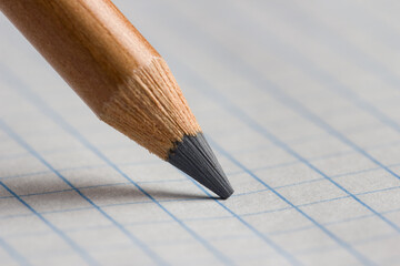 The tip of a pencil on a checkered paper in close-up.