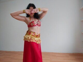A dancer in a red suit is dancing an oriental dance on a white background. Free space for text. Banner. A professional dancer dances oriental belly dance. Sexy woman in red dress dances a seductive