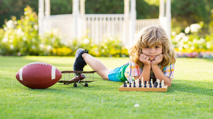 Dream kids and childhood concept. Concentrated child boy developing chess strategy, playing board game in backyard, laying on grass. - 786848924