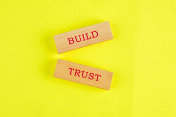 Build trust symbol on wooden blocks on a yellow background. Business concept