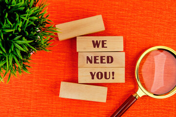 We Need You Message Concept on wooden blocks on a red background near a magnifying glass and...
