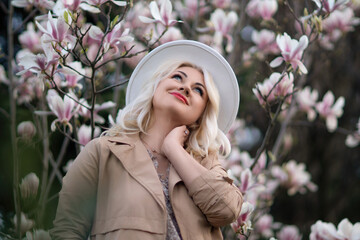Magnolia flowers woman. A blonde woman wearing a white hat stands in front of a tree full of pink...