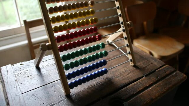 Brightly colored abacus on aged wooden desk, a symbol of traditional education and arithmetic. Essential for themes involving learning, counting, and historical teaching methods