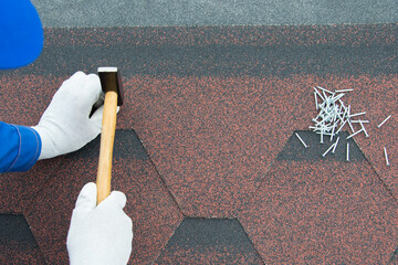 a worker repairs the roof with soft tiles, hammer in a nail