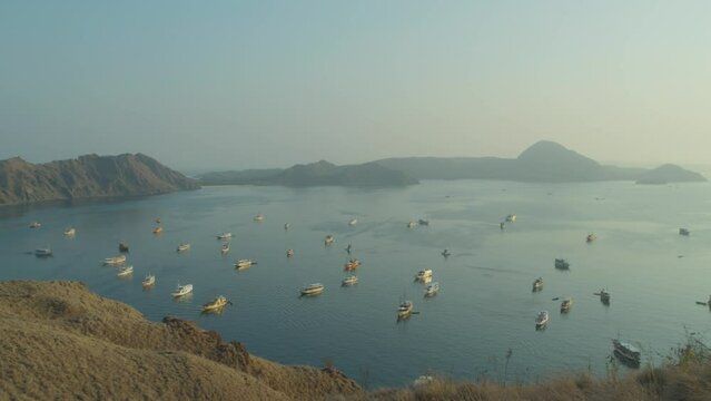 Many boats anchored in bay of Padar island, Indonesia. Pan right establishing shot.