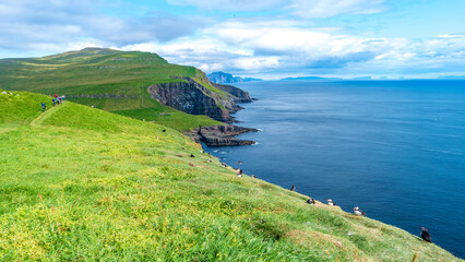 Mykines, Faroe Islands. Panoramic view of Mykines island, bird watching destination for puffins. Hikers at fjords landscape and seascape
