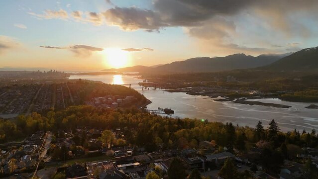 Panoramic aerial drone view (pan right) of the sunset over the skyline of Vancouver, Burnaby, and the Burrard Inlet during a spring season in British Columbia, Canada