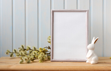 Easter mockup with an empty frame and an Easter bunny figurine on the table. Festive background.