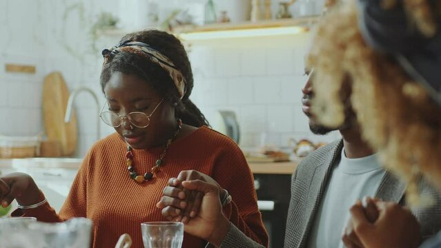 African American family members holding hands and praying with eyes closed before meal on holiday dinner at home