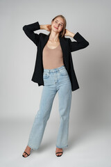 Young Woman Wearing Black Jacket and Jeans posing on gray background studio shot .