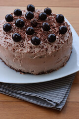 Close-up of whole chocolate cake with cocoa cream and sour cherries in syrup decoration on a white plate on wooden table