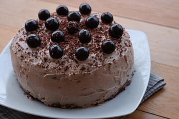 Close-up of whole chocolate cake with cocoa cream and sour cherries in syrup decoration on a white plate on wooden table