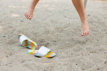 Barefoot girl with flip flops in sand