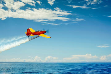 A small red plane is flying over the ocean