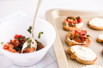Bruschetta being topped with tomates and basil