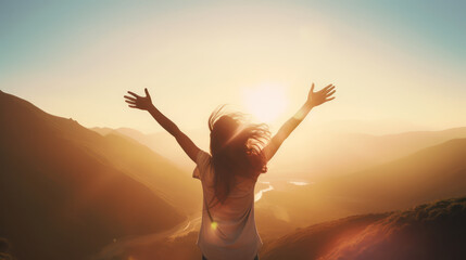 Young woman with arms raised in joy, embracing the sunlight on top of mountain at sunrise.