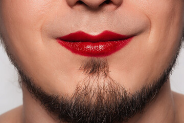 Closeup of handsome bearded man getting makeup. Paints lips lipstick in a red color