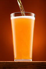 a glass of beer on a wooden stand and a light brown background, pouring beer into a glass, a close view of the object, the beer foams up and bubbles