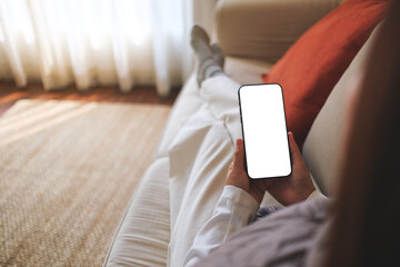 Mockup image of a woman holding mobile phone with blank desktop white screen while sitting on a sofa at home - 786899948