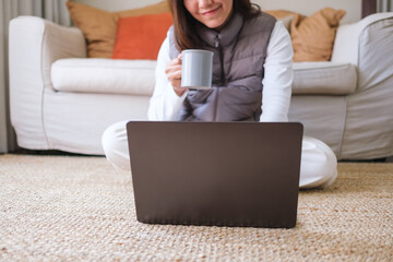 Closeup image of a young woman drinking coffee while working on laptop computer at home - 786900105