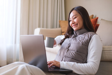 Portrait image of a young woman drinking coffee while working on laptop computer at home - 786900133