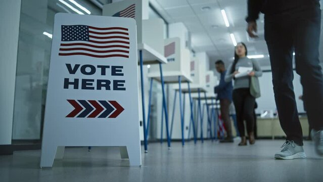 Vote here sign on the floor. Multi ethnic American citizens vote in booths in polling station office. National Election Day in United States. Political races of US presidential candidates. Civic duty.