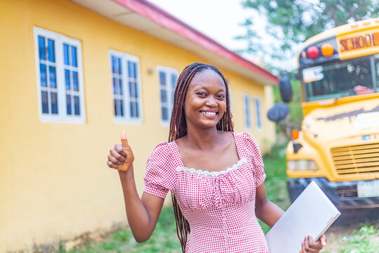 Excited African-American Student with Laptop by School Bus, Thumbs Up