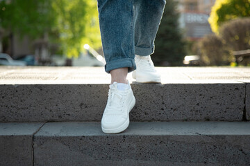 Female legs in  white summer   sneakers and rolled up jeans descending the stairs in the city . Front view