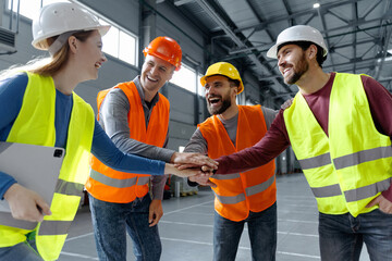Successful team, managers, engineers wearing hard hats, work wear and vests holding hands together