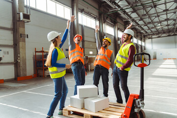Successful team, managers, engineers wearing hard hats, work wear and vests working in warehouse