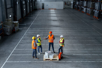Top view, group of factory workers wearing hard hats, work wear, vests standing near pallet truck
