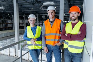 Successful confident workers, engineers wearing hard hats and work wear looking at camera
