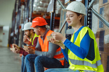 Young woman worker, engineer wearing hard hat, vest and work wear holding lunch, eating during break