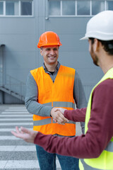 Handsome, smiling men, workers wearing hard hats, vests shaking hands, making deal