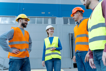 Group of professional smiling workers, engineers wearing hard hats, vests talking, planning project